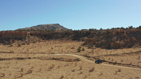 aerial as car drives down rugged dirt road through desert with rock formations