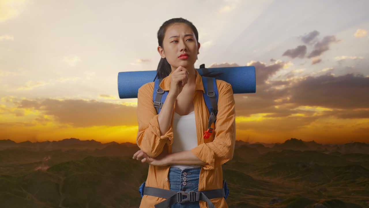 excursionista asiática con mochila de montañismo pensando en algo y mirando a su alrededor luego levantando su dedo índice mientras está de pie en la cima de la montaña durante la hora del atardecer