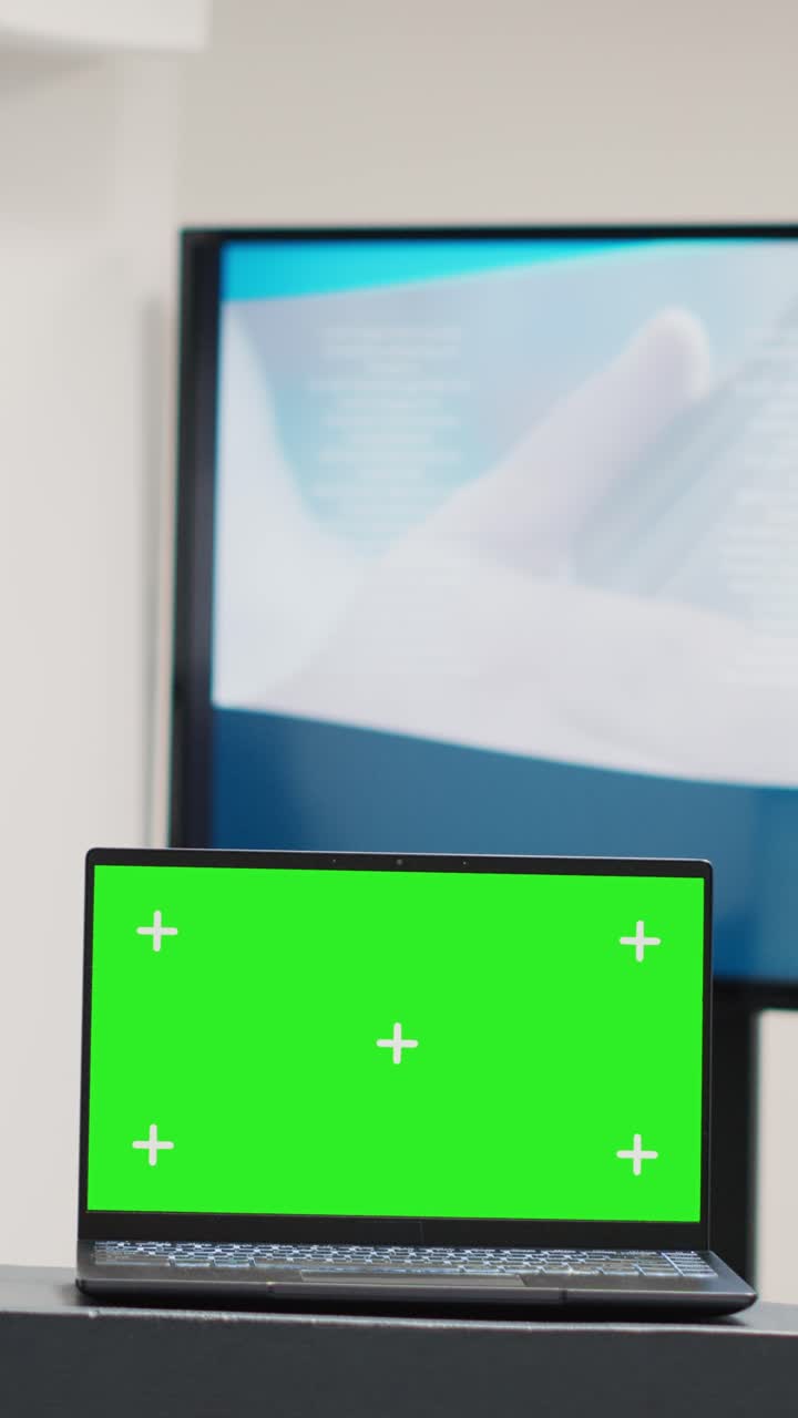 Vertical video: Laptop with greenscreen display at desk