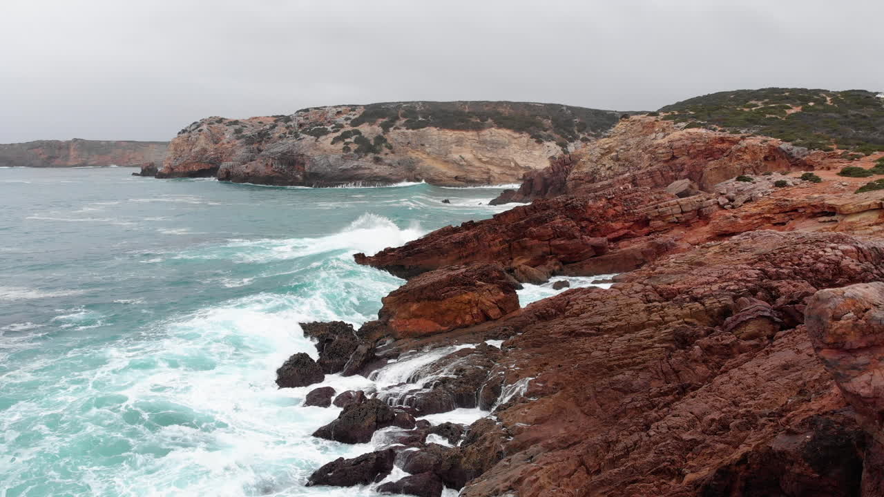 AERIAL: flying over the coastline while waves crash into the rocks