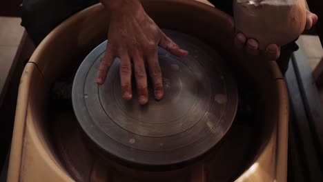 a man moistens a potter's wheel with water and throws a lump of clay on it.