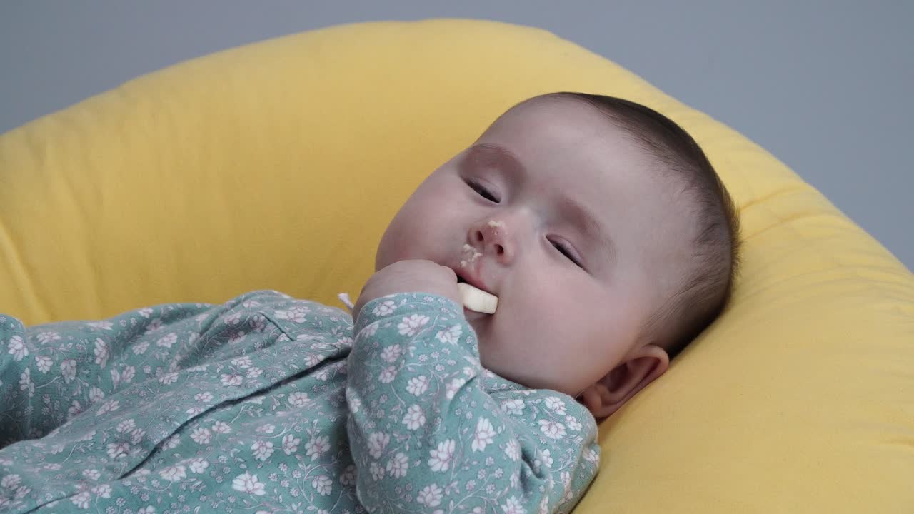 Baby Eating A Biscuit While Lying On A Yellow Foldable Bed