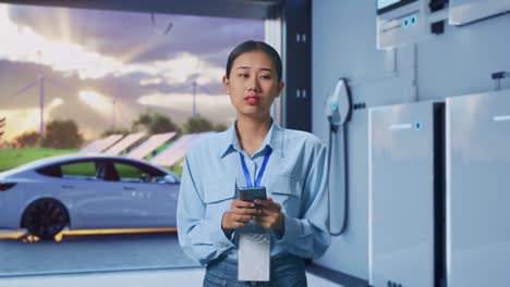 Asian Female With Her Smarphone With Home Energy Storage System In a Modern Garage, She Observes By Looking Around Before She Come To Concentrating With Her Smarphone