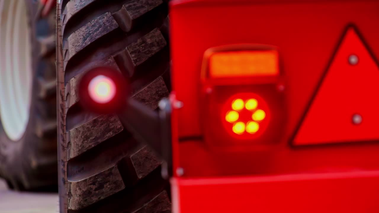 Rack focus from thick tractor tire to flashing red danger light on back of heavy machine