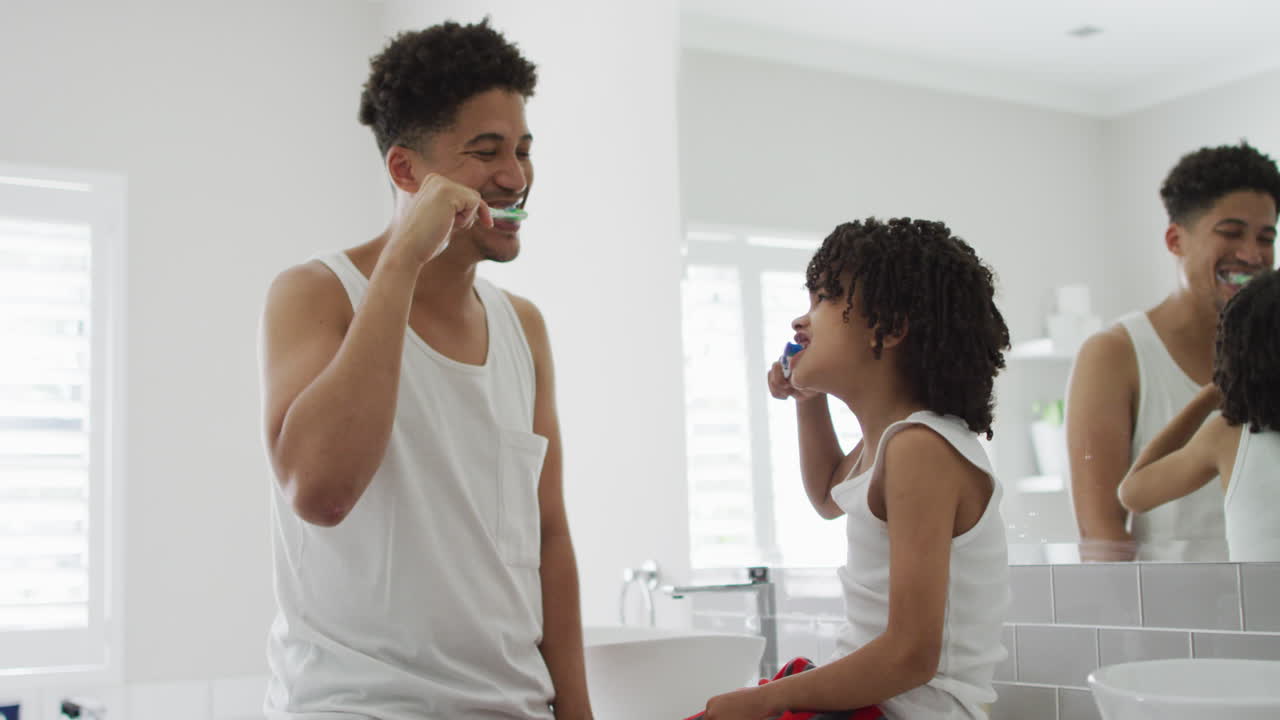 Biracial father and son brush their teeth together at home