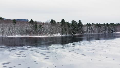 Aerial-SLIDE-past-shore-and-the-pockmarked-ice-next-to-open-water-in-early-winter