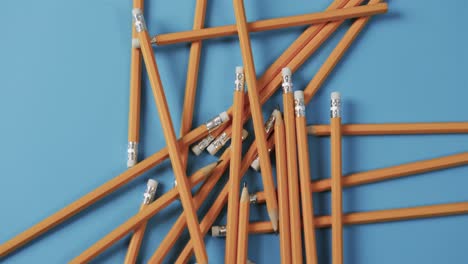 Overhead-view-of-scattered-pencils-with-blue-background,-in-slow-motion