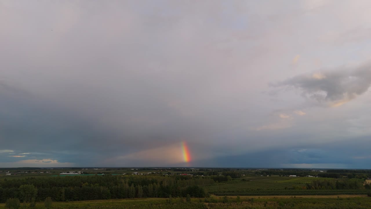 Aerial view of rainbow over green field with dramatic rain clouds. Peaceful and vibrant nature scene, perfect for weather, landscape, and travel visuals