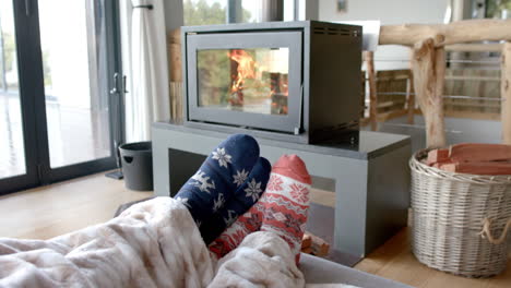 Füße-Eines-Paares-Auf-Dem-Sofa-In-Warmen-Socken-Unter-Einer-Decke-Vor-Dem-Kamin-Zu-Hause,-In-Zeitlupe