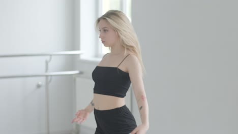 fit girl in black clothes performing contemporary. female dancer shows flowing motions, body and hands waves at white room. modern ballet dance choreography. young woman is moving smoothly