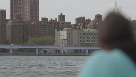 rack focus shot of woman enjoying being outside, as she looks out over the east river across from lower manhattan