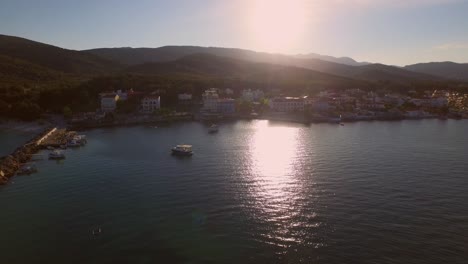 Aerial:-Small-fishing-town-with-Greek-flag-on-Samos-island,-Greece