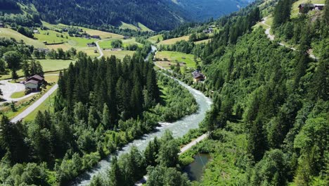 drone of an alpine river meandering through vibrant green mountain summer fields