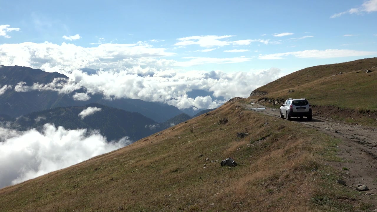 SUV argentato che guida su una strada sterrata di montagna sopra le nuvole.