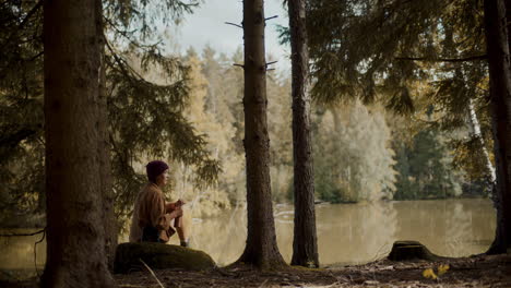 Female-tourist-sitting-on-rock-by-lake-in-forest