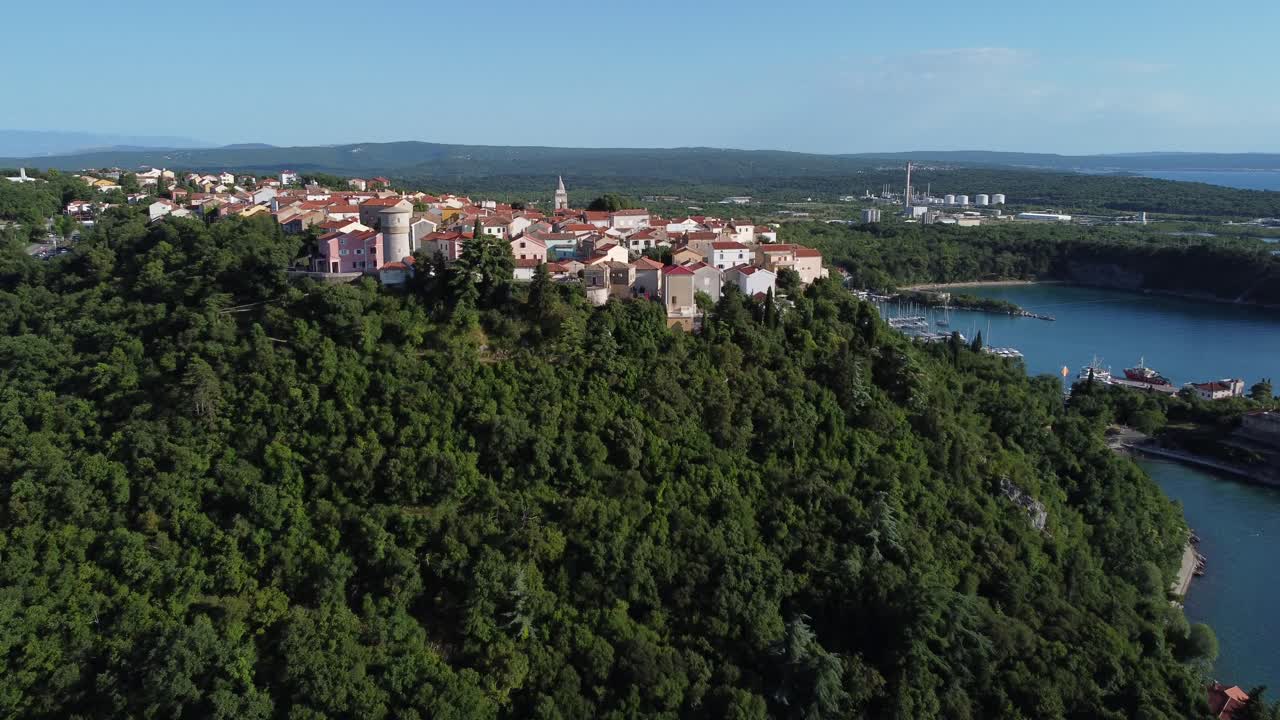 drone acercándose a la antigua aldea en lo alto de la colina en krk croacia con casas, bosques y bahía en el fondo