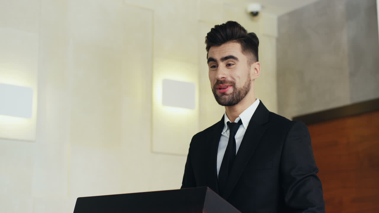 vista de cerca del orador de un hombre de negocios barbudo caucásico en un podio usando ropa formal y hablando en una sala de conferencias