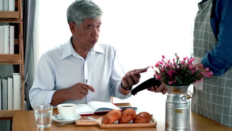 active senior asian man working in a coffeeshop using a mobile device, smartwatch for nfc, qr code scanning, contactless payment to pay for coffee and snack