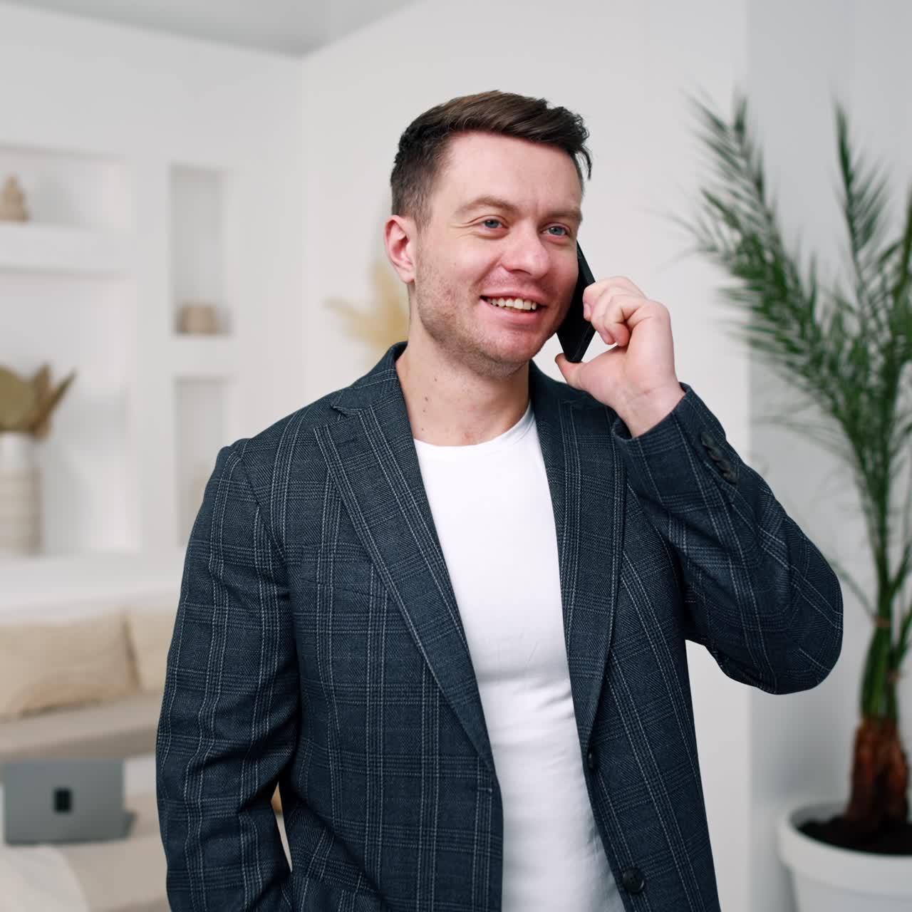 Pozitivní, pohodový muž telefonuje. Muž kavkazského vzhledu v bundě komunikuje s klienty z domova.