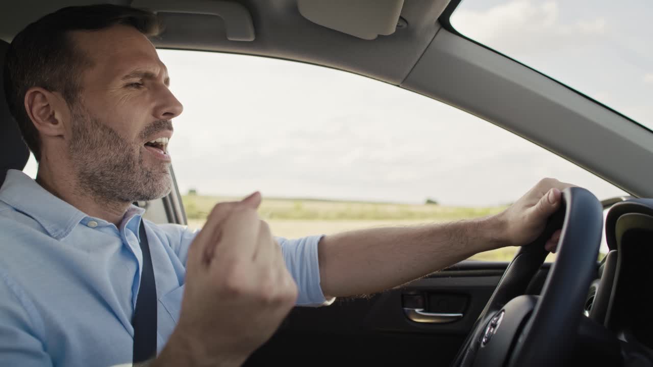 hombre caucásico de mediana edad conduciendo un coche y cantando.