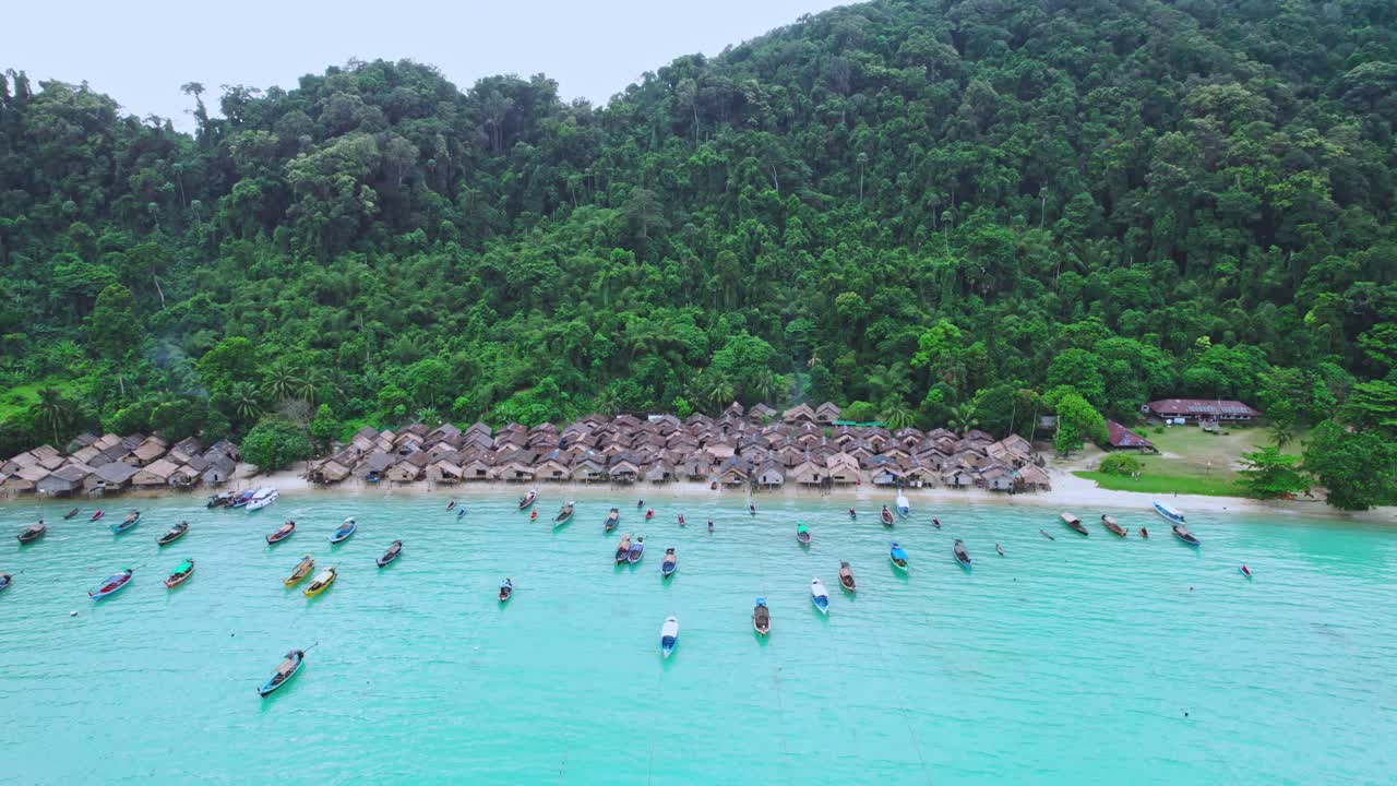 목조 오두막이 있는 해안 해변 마을을 따라 긴 리 보트, 약간의 비가 내리는 공중 드론 리