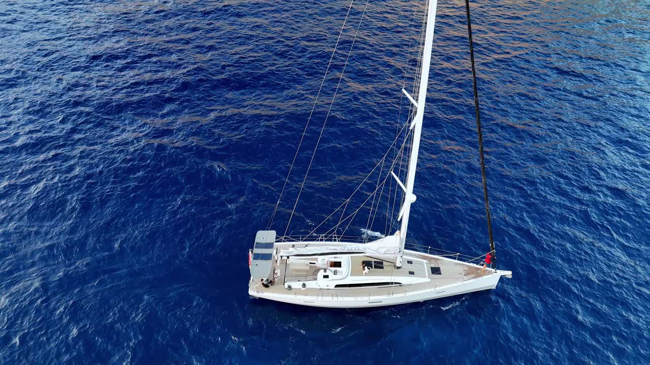 Vista aerea da drone di un lussuoso yacht a vela che naviga nelle acque blu intenso del Mediterraneo vicino alle frastagliate scogliere costiere di Gozo durante un luminoso pomeriggio estivo nell'arcipelago maltese