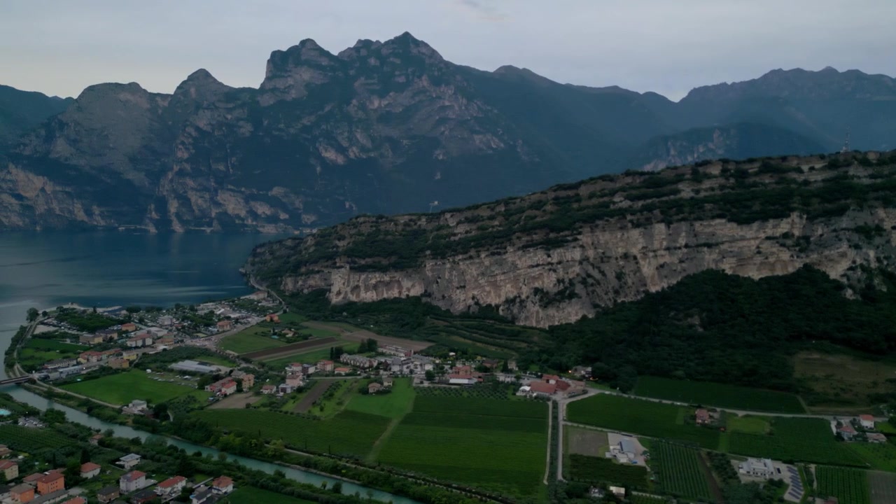 Veduta aerea che sorvola campi verdi con scogliere imponenti e una città lacustre in lontananza.