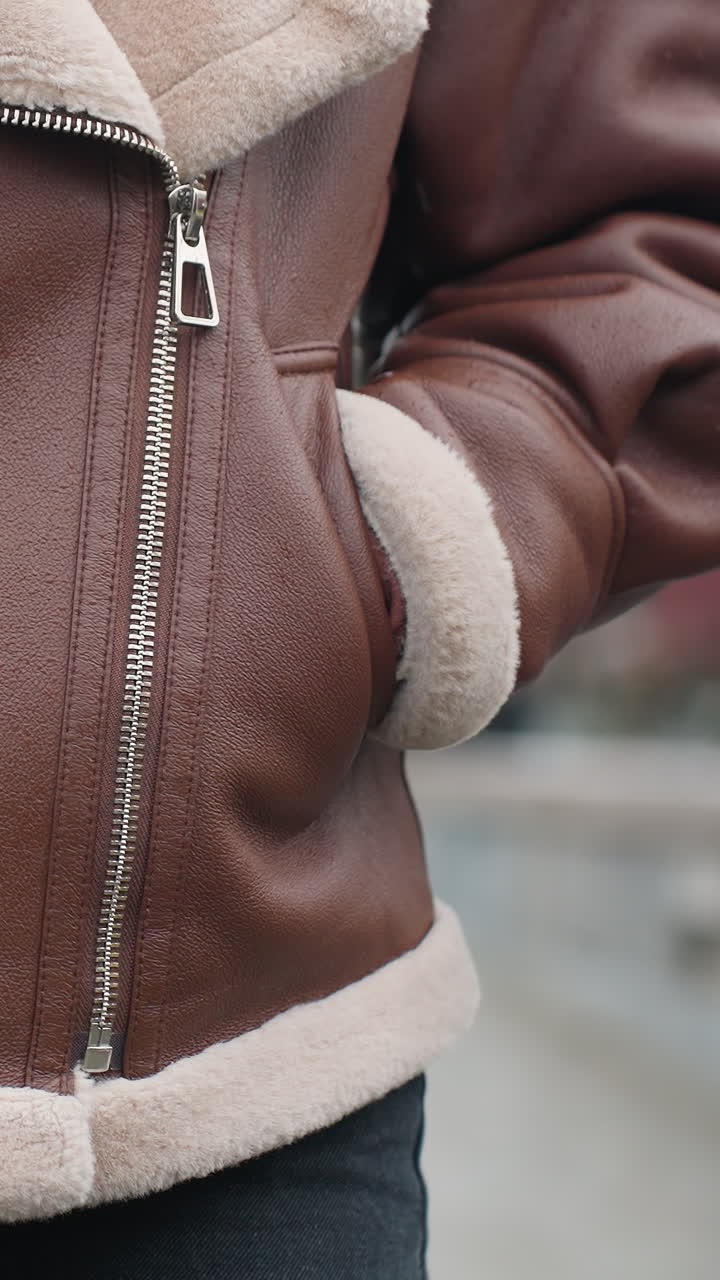 Front shot of person's brown shearling jacket with hands tucked in pockets, face not visible, showing cozy texture and design of warm winter outerwear worn outdoors on chilly day