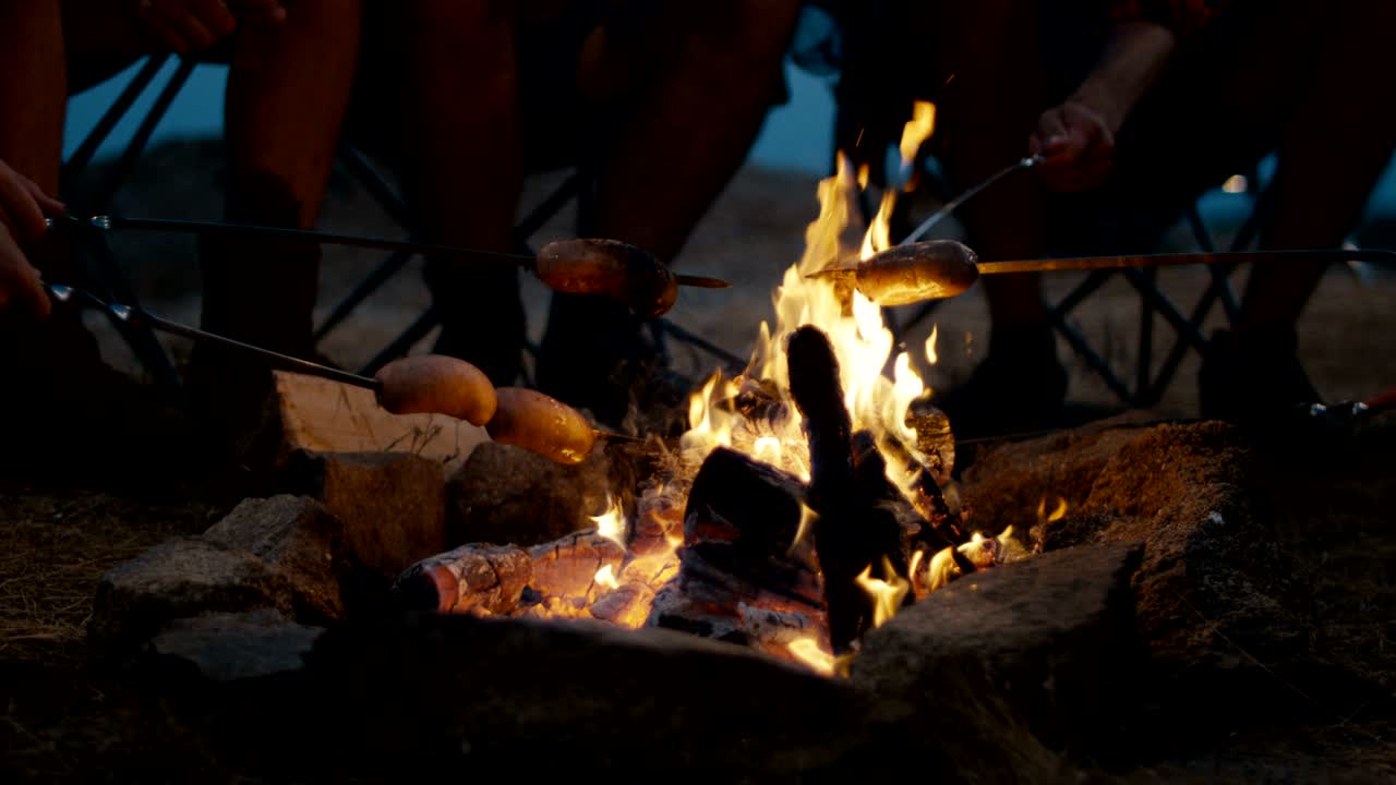Crop people frying sausages in bonfire
