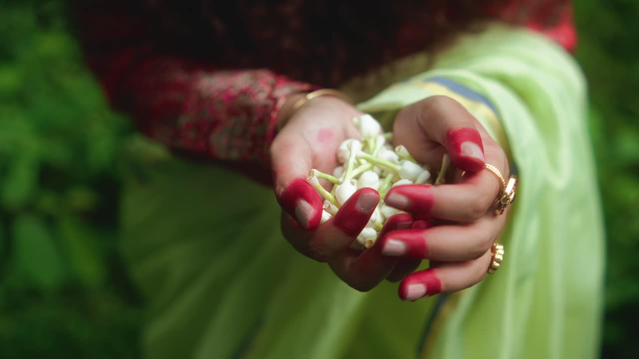 A gentle hand delicately holds a small bouquet of wildflowers, surrounded by lush greenery and soft natural light. The scene captures a peaceful moment of connection with nature and simple beauty