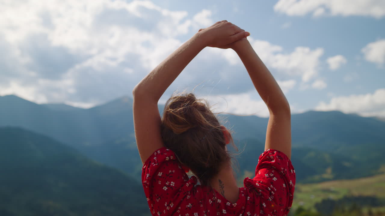vista de atrás mujer despreocupada con las manos sobre la cabeza relajándose en las montañas de cerca.