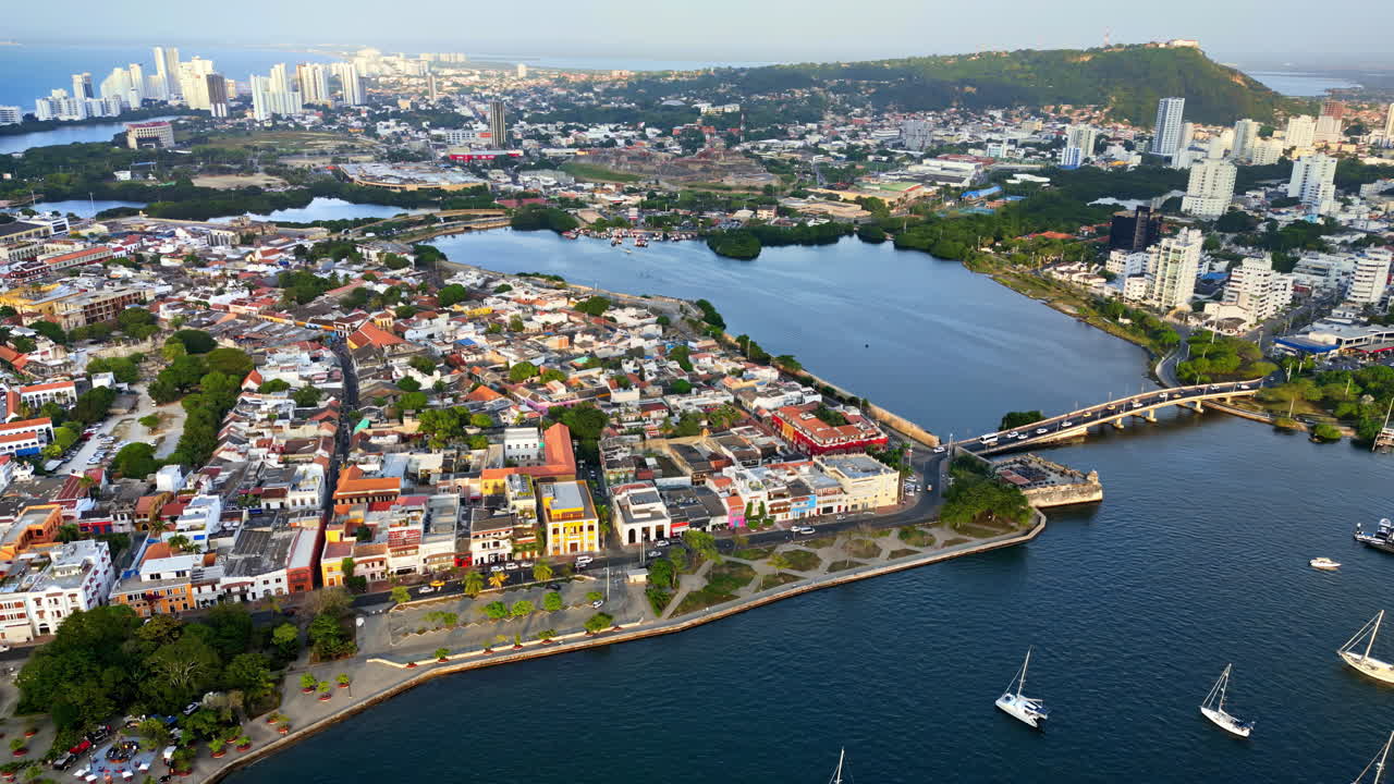Aerial drone view of Cartagena's colonial old town surrounded by the sea, with yachts anchored in the bay and the modern skyline in the distance
