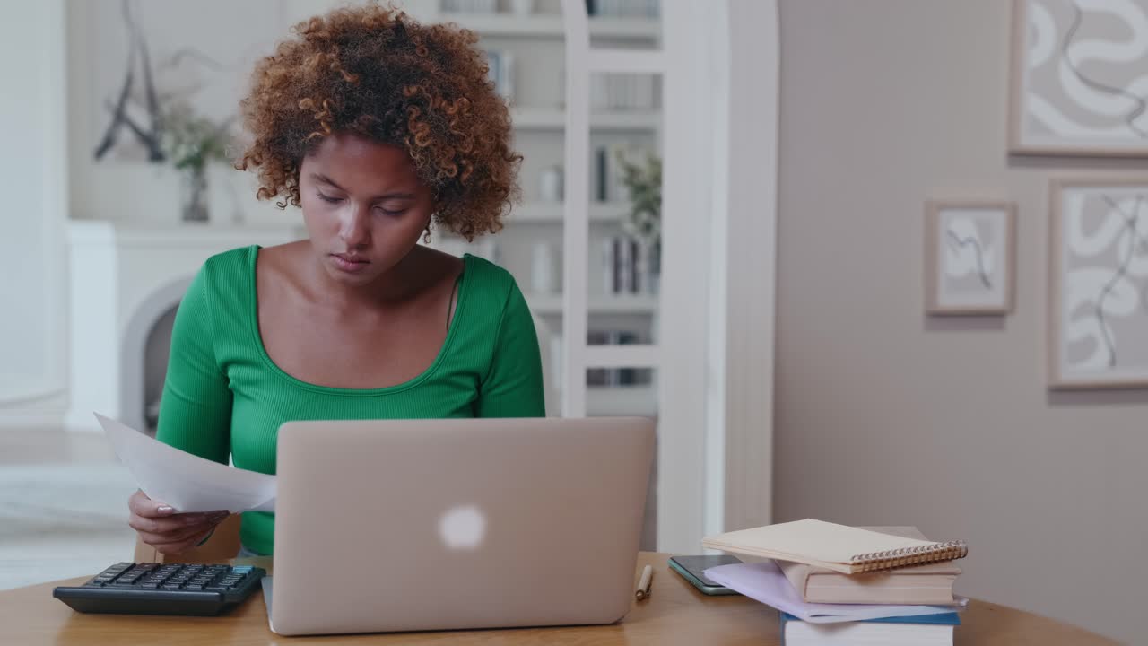 Young african american woman accountant uses calculator sits at desk with laptop
