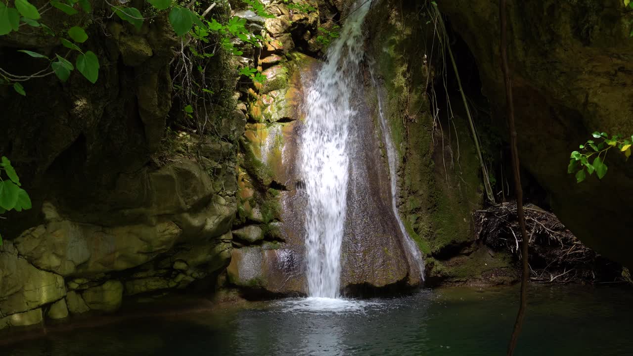 la luz del sol brilla en la cascada de kefalogourna, rodeada de vegetación verde y rocas musgosas, isla de thassos, grecia