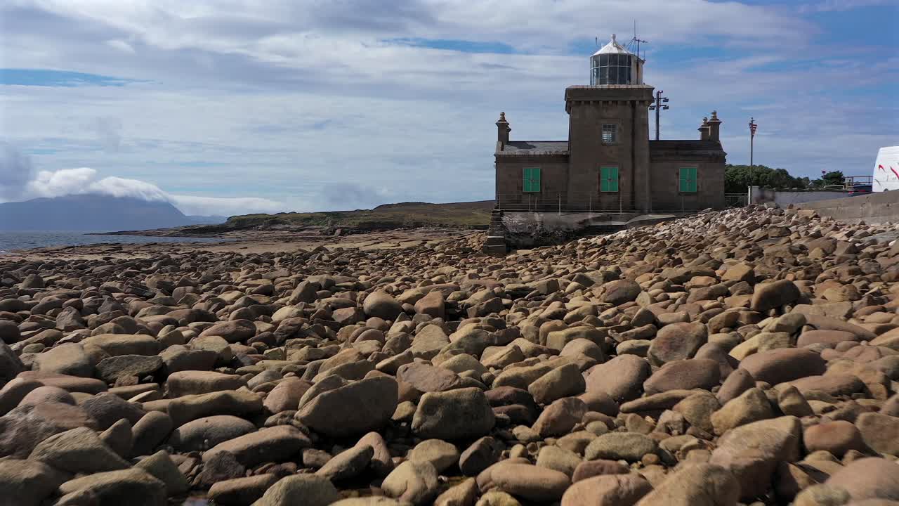 Lenta carrellata aerea verso il Faro di Blacksod mentre le rocce in primo piano creano profondità e scala, County Mayo