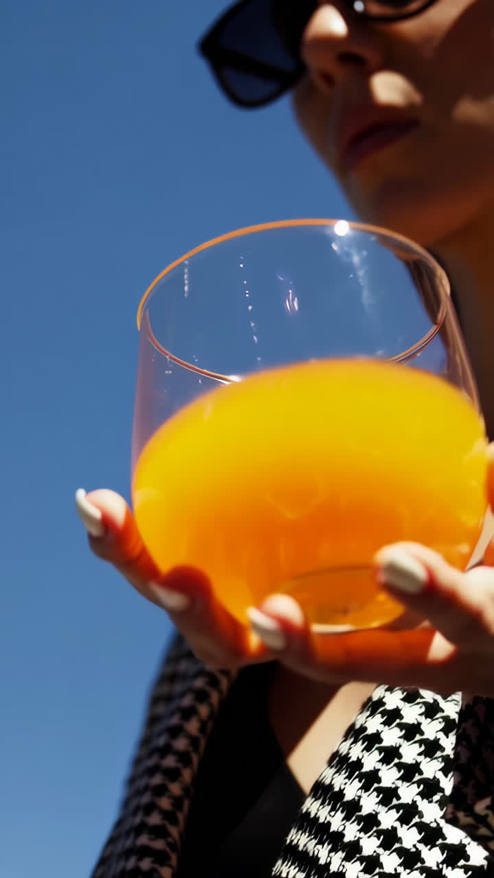 Hand holding a refreshing drink against a clear blue sky with houndstooth fabric