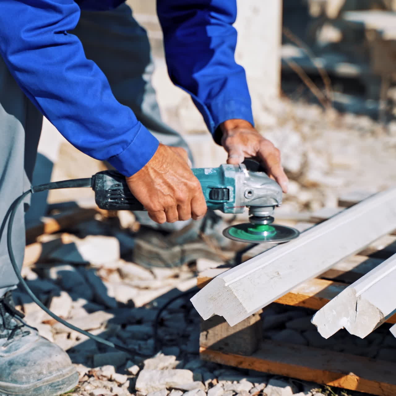 Laborer polishes stone with hand grinder outdoors. Man worker is polishing stones by hand grinding machine on the open air.