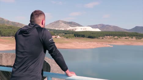 Man-standing-on-the-fence-of-a-dam-enjoying-the-view-of-the-lake