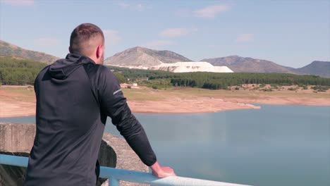 hombre parado en la valla de una presa disfrutando de la vista del lago