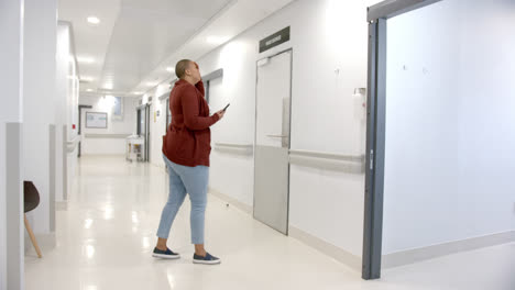 stressed african american woman using smartphone in hospital corridor, slow motion