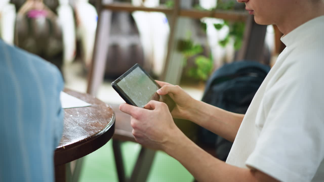 Camera pans across indoor scene revealing wooden pillar obscuring view of young man seated with head down on table in contemplative posture subtle motion adds dramatic obstruction effect mood depth