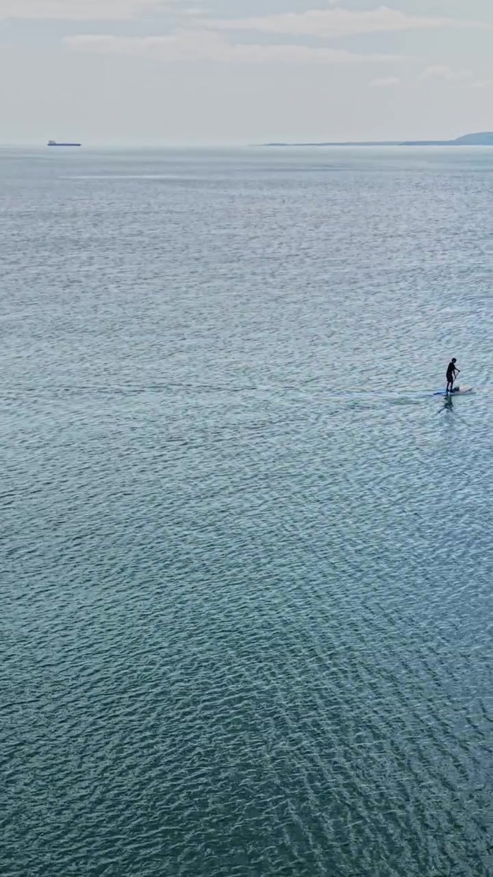 Persona che fa paddleboarding su acqua calma con navi in lontananza.