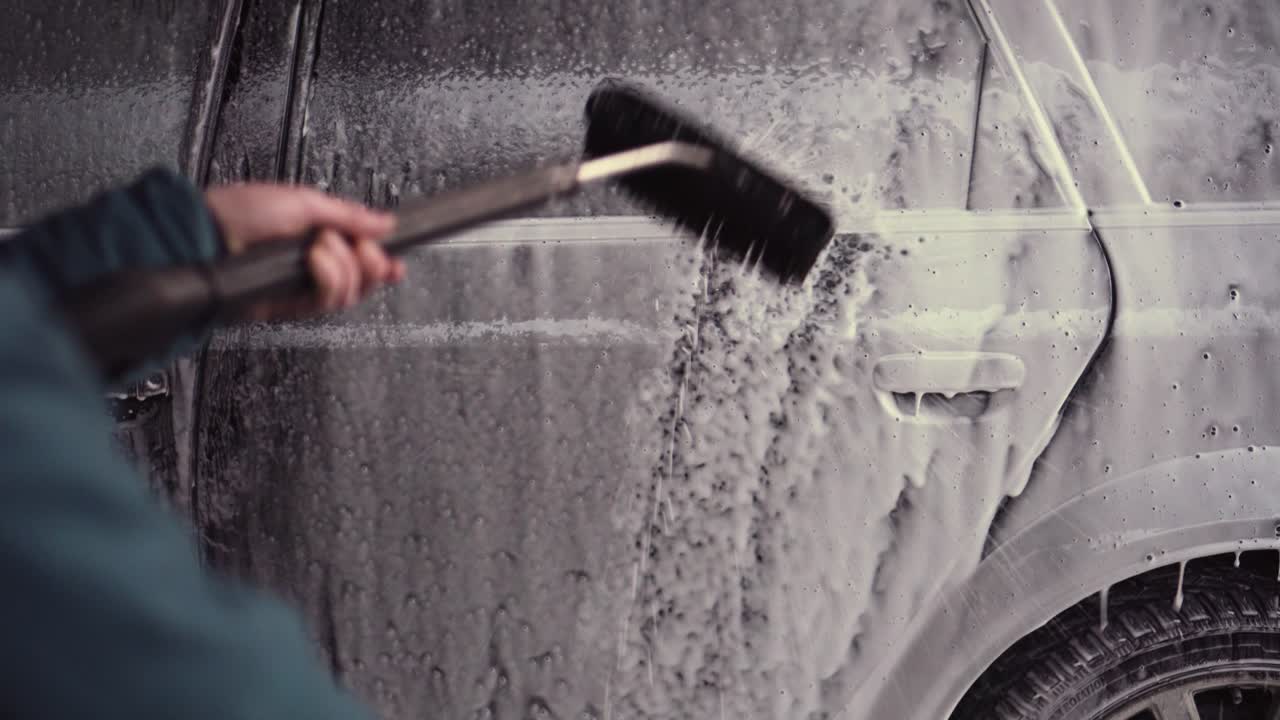 Person holding water pressure washer with brush, touchless car wash