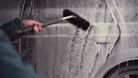 person holding water pressure washer with brush, touchless car wash