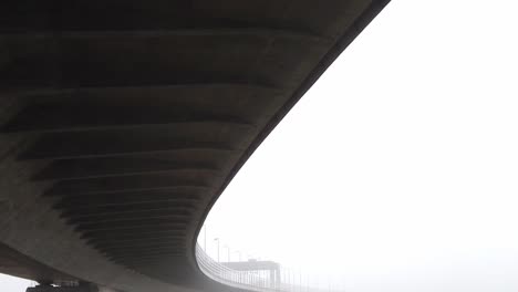 debajo de una gran infraestructura de autopista de hormigón curvo que se inclina hacia el brumoso y siniestro paisaje del paso elevado
