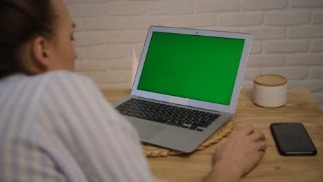 green computer screen. the girl sits at the table and remotely learns, works. surfs the internet. a girl in a striped pajama top. rear view.
