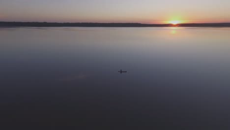 aerial flying around fisherman in a boat on a lake on a calm summer evening at sunset