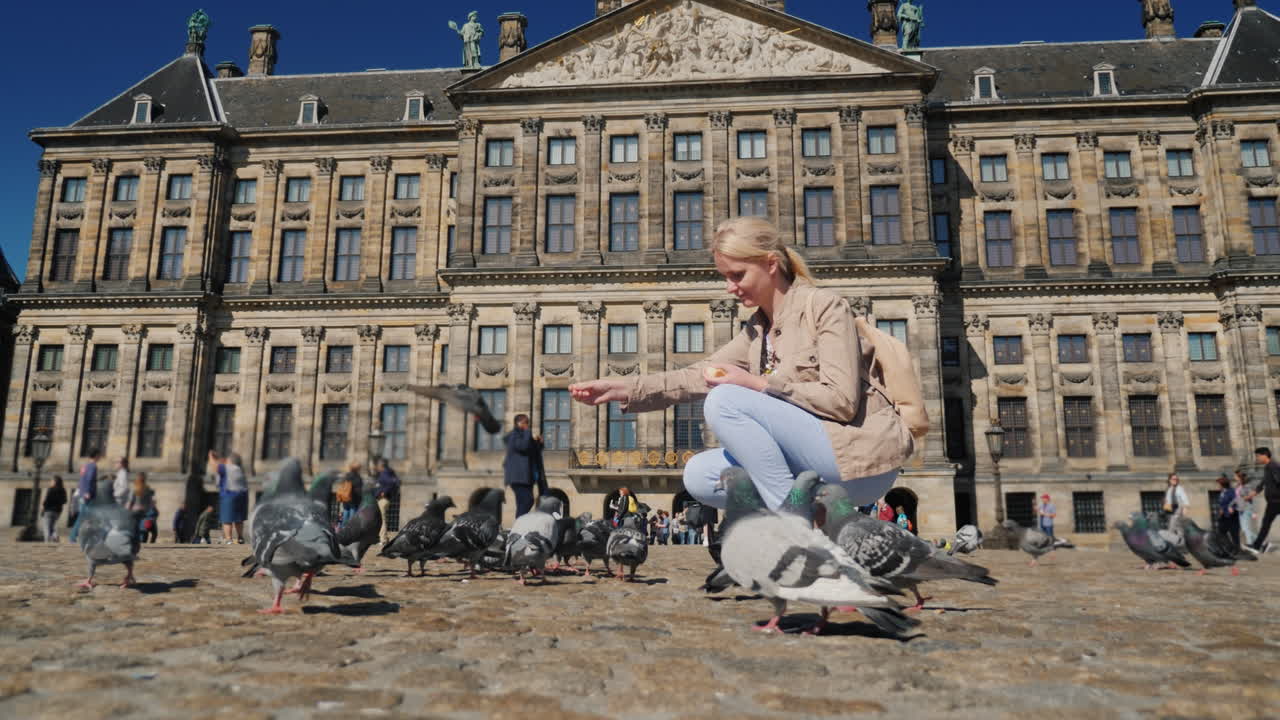 여자가 댐 광장에서 비둘기에게 먹이를 주고 있다