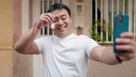 young chinese man holding key of new home having video call at street