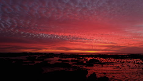 Tiro-Inclinado-Hacia-Arriba-De-La-Vívida-Puesta-De-Sol-Que-Ilumina-Las-Nubes-En-La-Costa-Rocosa